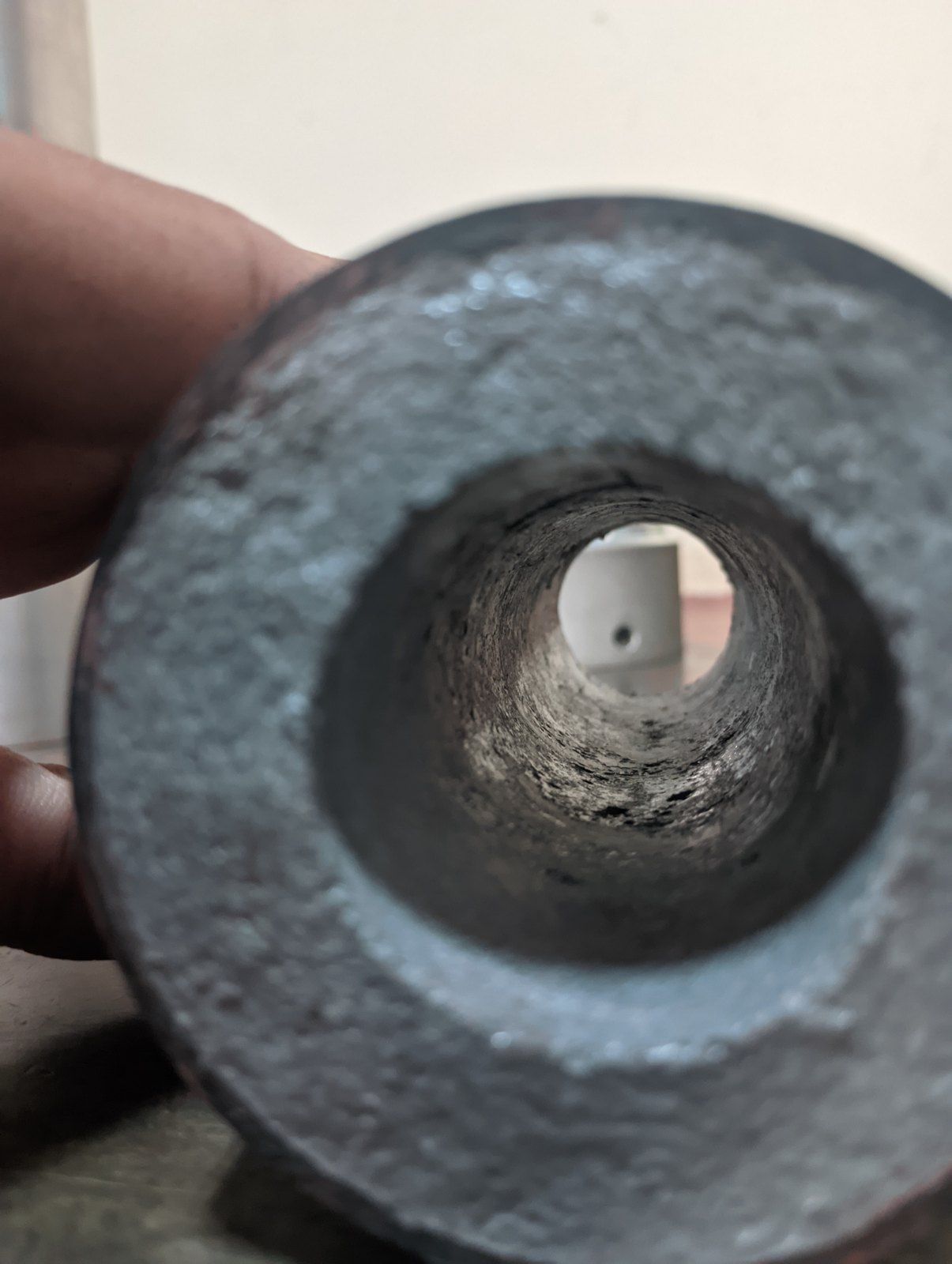 A hand holding a grey cast propellant grain end-on, showing a rough, uneven central bore.