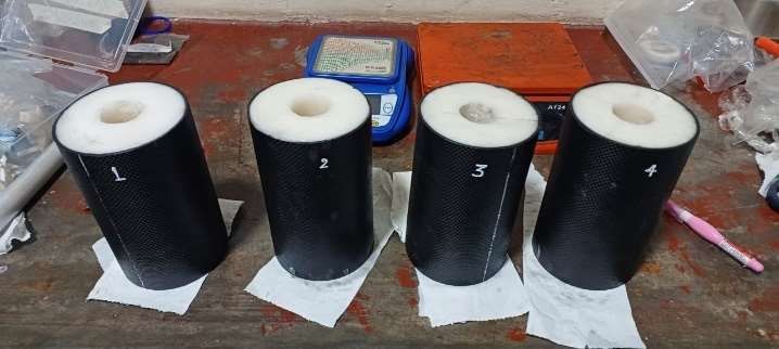 Four cast propellant grains in black liners, numbered 1 to 4, standing on paper on a workbench
